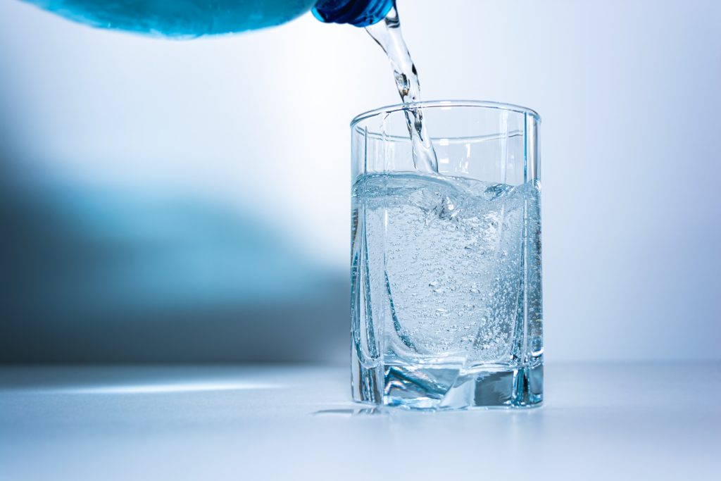A clear bottle of distilled water pours smoothly into a drinking glass, illustrating clean, purified hydration for everyday use.