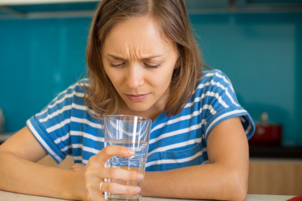 A woman looking disapprovingly down at her glass of water demonstrating how homeowners do not want PFAS in their water.